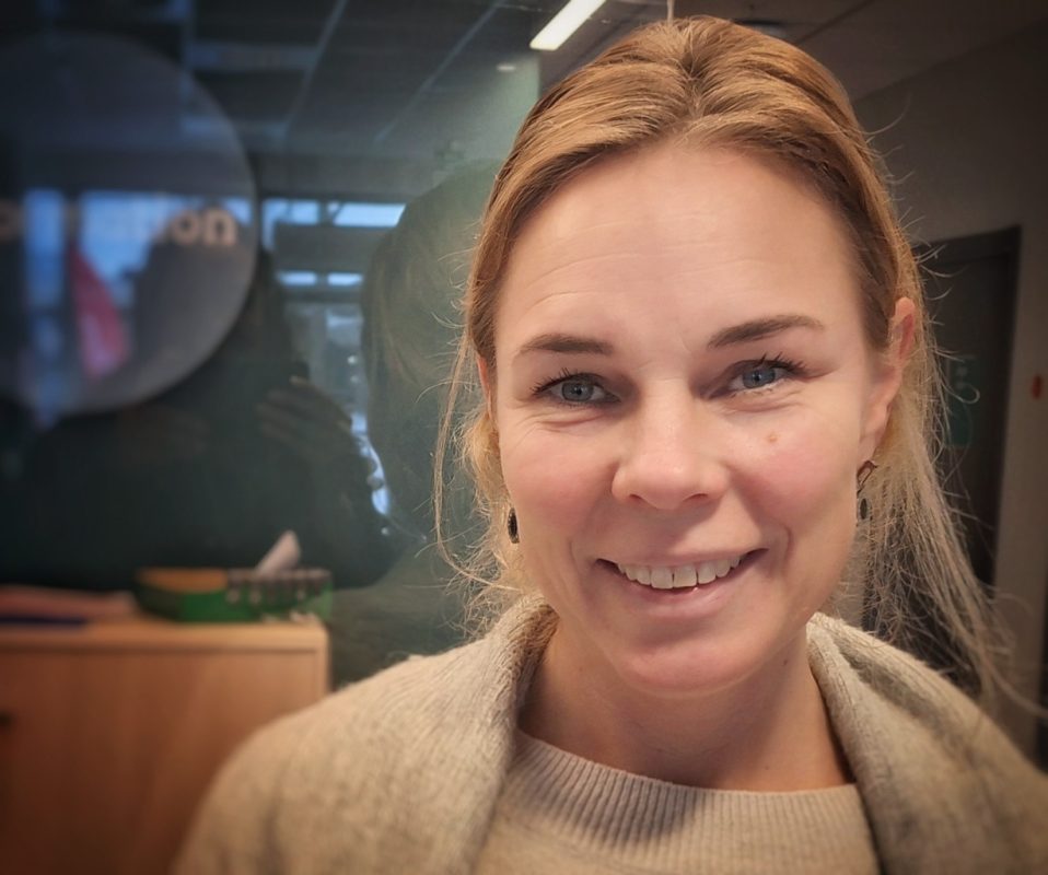 En vit kvinna i ljust hår, med vit tröja och kofta.