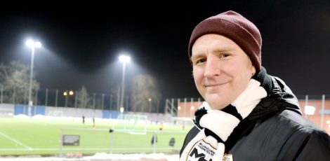 glad medelåldersman med mössa och en fotbollsplan