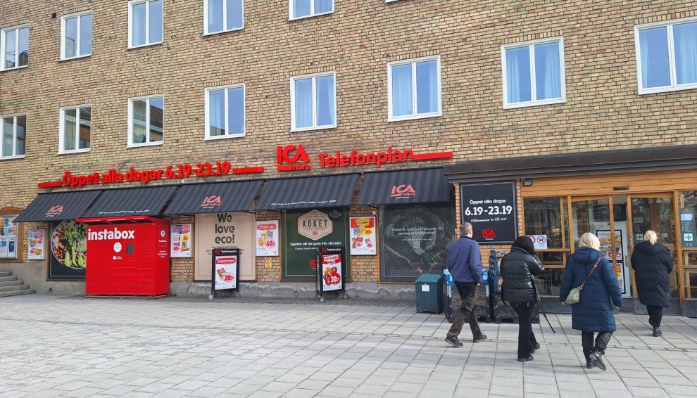 En beige tegelbyggnad med två rader med fönster. I nedrbotten en butik med svart fasad och röda skyltar.