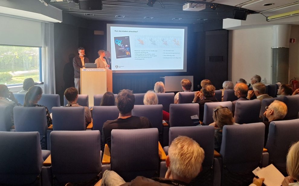 Auditorium med blå fåtöljer och ett pdie samt vit projektion i mitten.