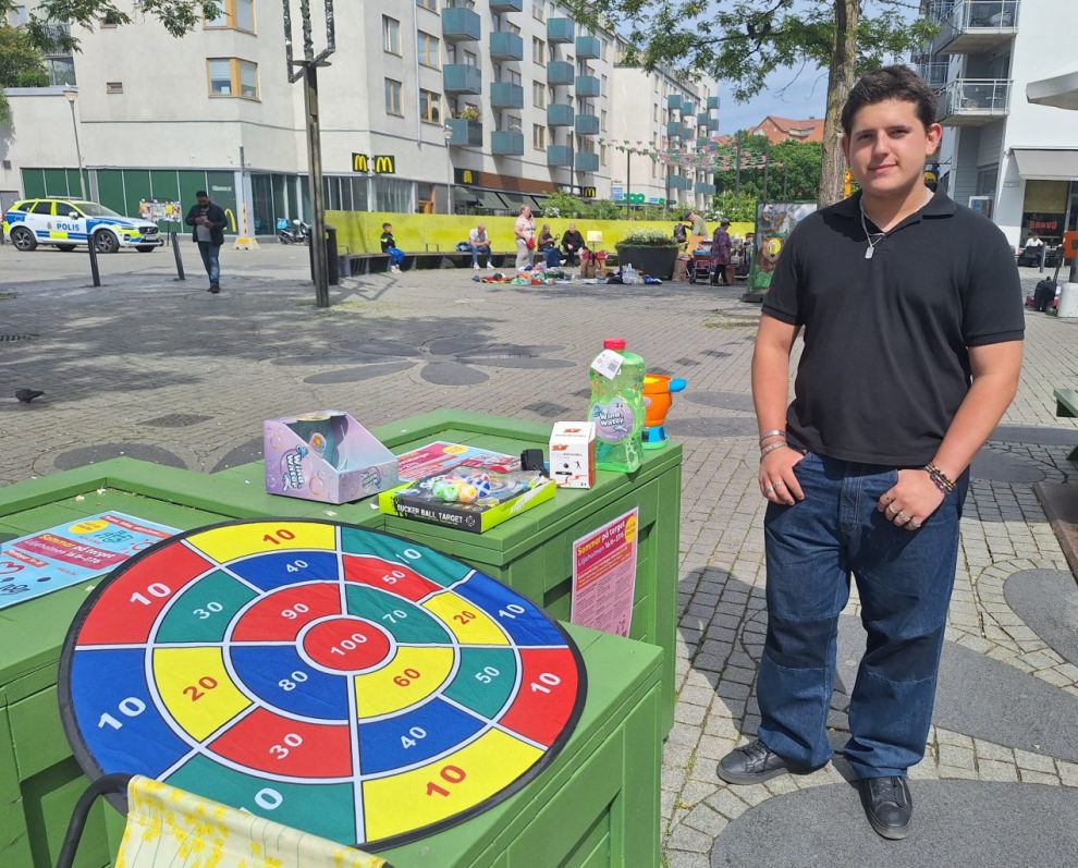 En icke vit, ung man  med mörkt kort hår står i svart t-shirt och jeans framför ett bord med leksaker.