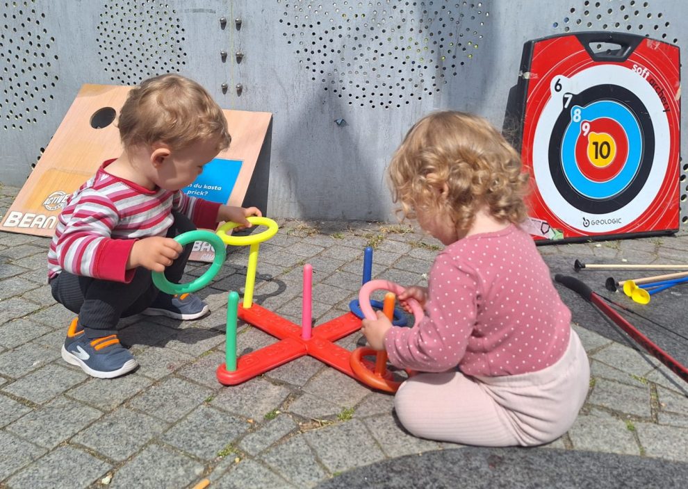 två små barn sitter och leker på marken med ringar i olika färger.