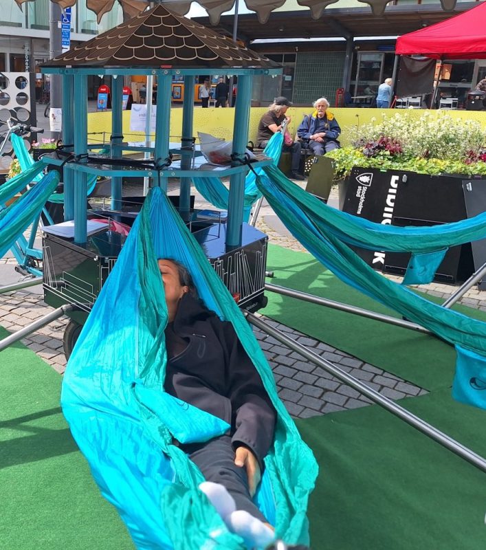 En brun kvinna har lagt sig i en turkos hängmatta. Hon har svarta kläder på sig och bara halva ansiktet syns bakom tyget.