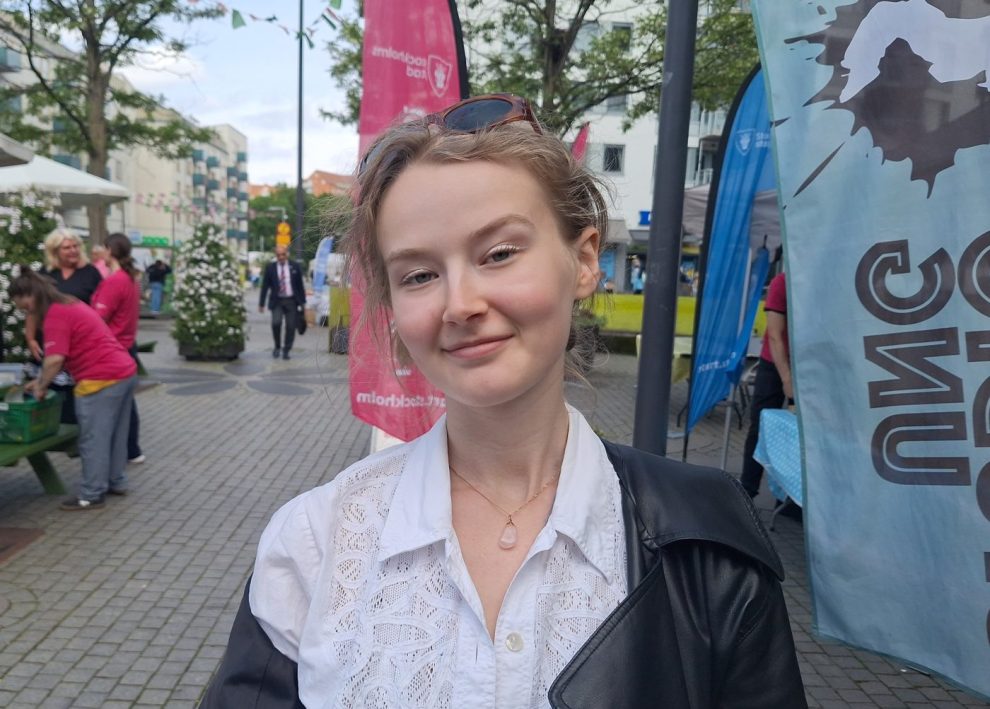 En vit kvinna med cenréfärgat hår i knut, vit blus och svart kofta.