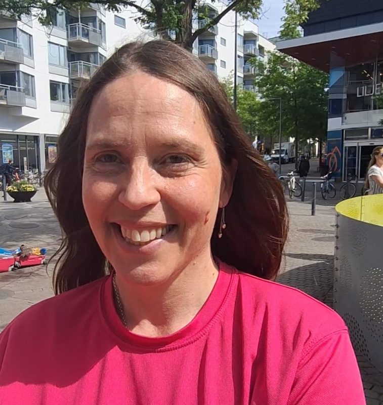 Vit kvinna med utsläppt långt mörkt hår och rosa t-shirt.