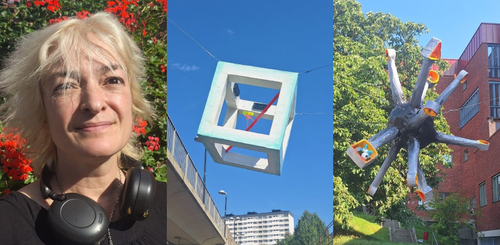 En icke vit kvinna i blonderat hår och svart blus, ett konstverk i form av en ljusblå ihålig kub, ett annat konstverk som ser uta som en svart explosio.
