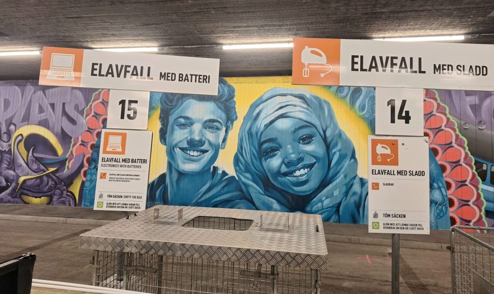 Vita skyltar med svart text: elavfall. I bakgrundenväggmålning som visar två barn, målat med stark turkos färg. bilder på 