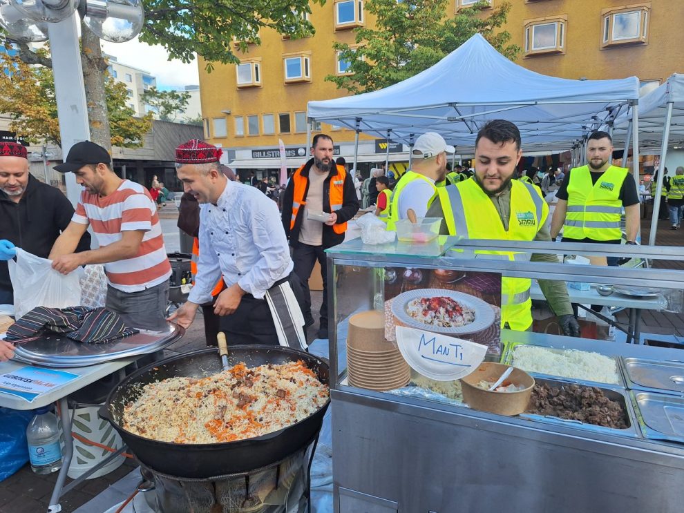 Män i gula västar bakom diskar med varm mat, en stor gryta med ris.