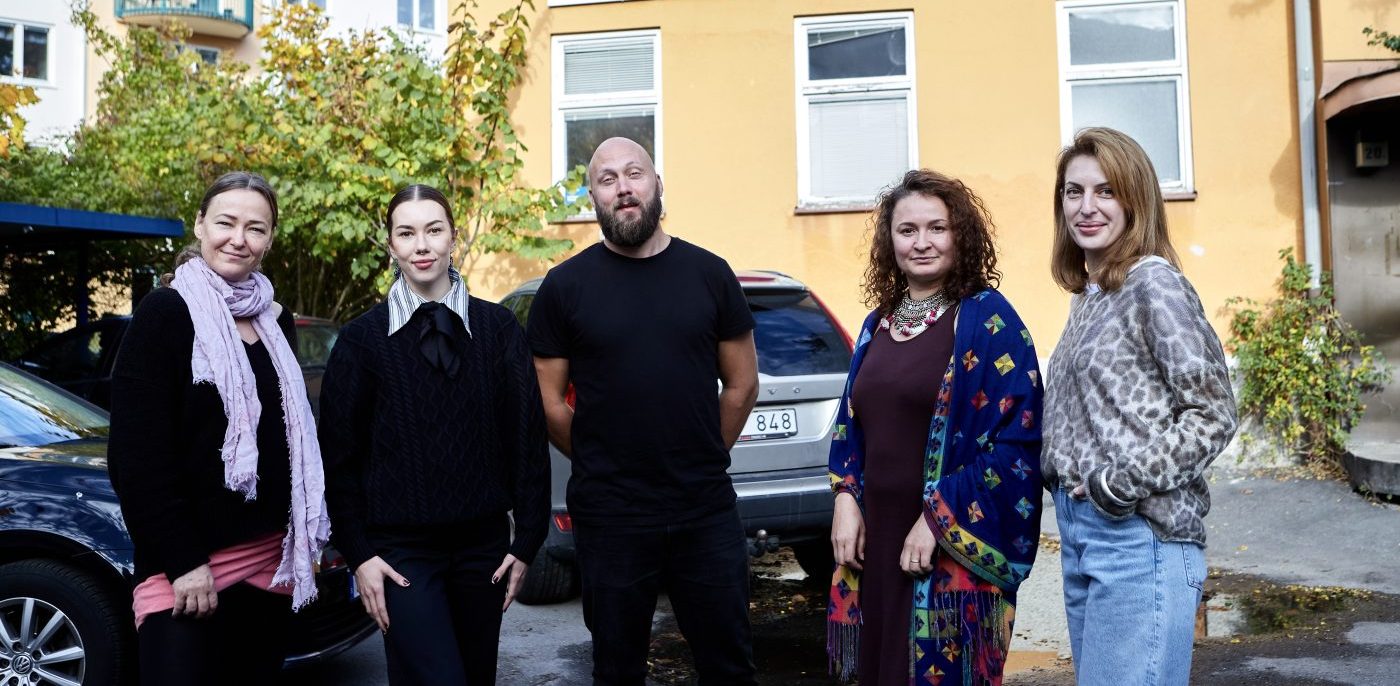 tre kvinnor och en man i 30- till 40-årsåldern, framför en gul tegelbyggnad, omgiven av en höstmässig grönska