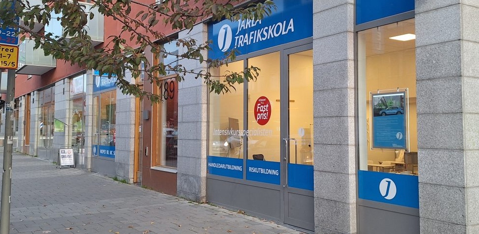 Ett skyltfönster med blå reklam, utanför en trottoar med träd.