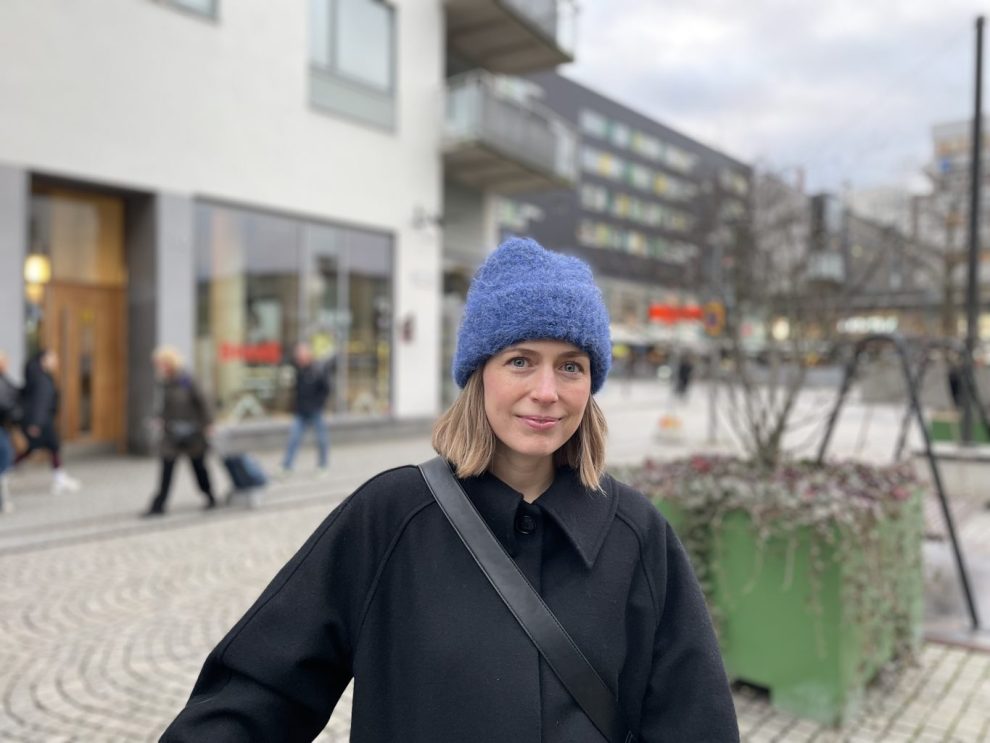 Vit ung kvinna med blont hår och ljusblå mössa och svart jacka.