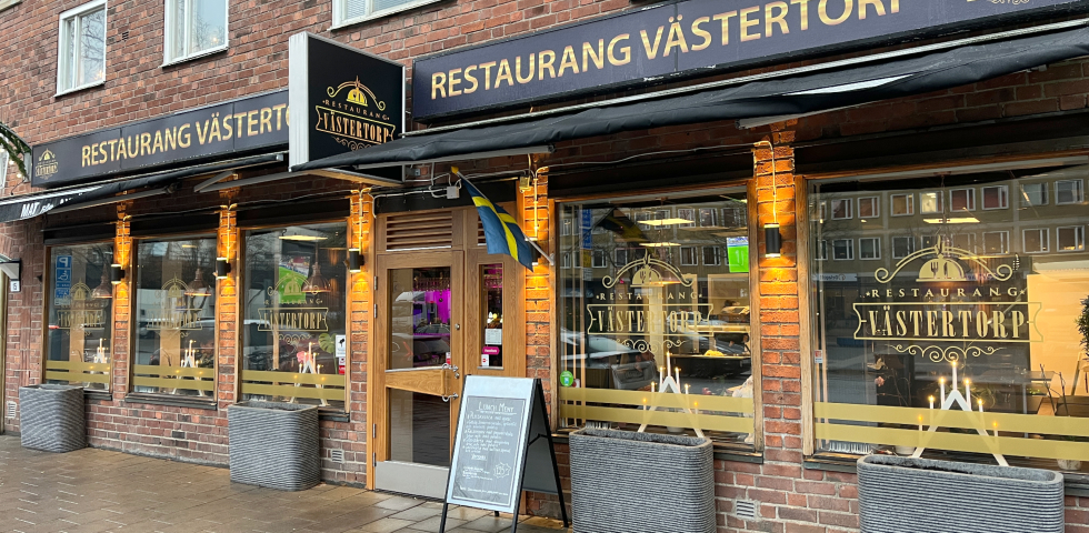 En bild på en restaurang sedd från trottoaren med adventsstakar i fönstren.