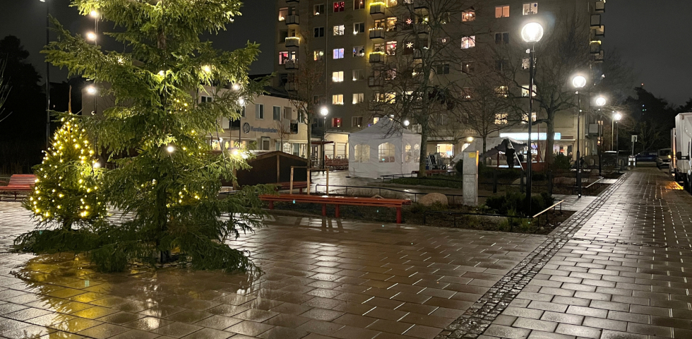 En bild på ett torg med två vita tält varav ett håller på att fällas ned. En julgran syns vid sidan om torget.