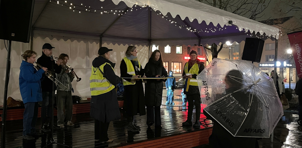 En bild på en scen med tre personer med blåsinstrument och två kvinnor med varsin sax liggandes mot ett band som två andra personer håller.