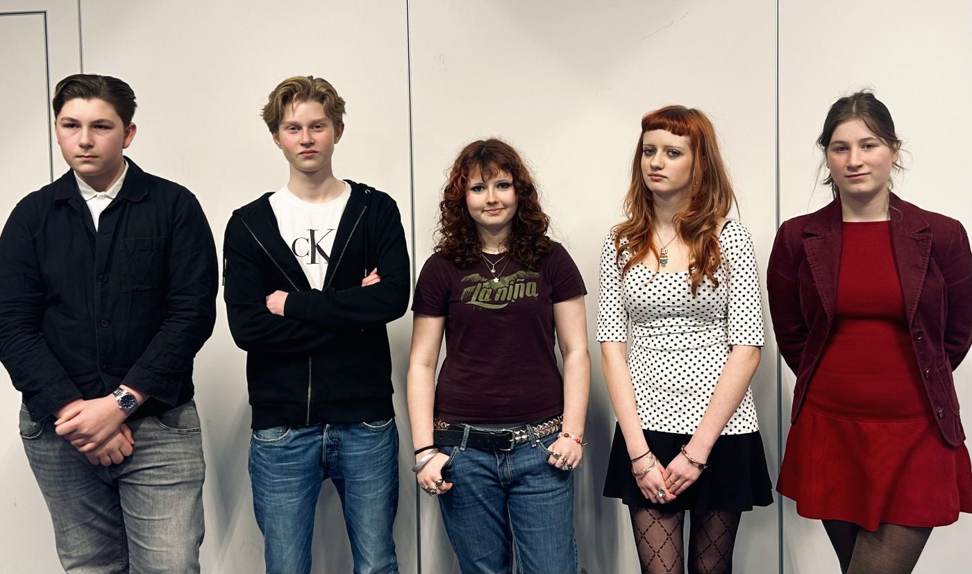 Fem skolungdomar i nionde klass står framför en vit vägg.