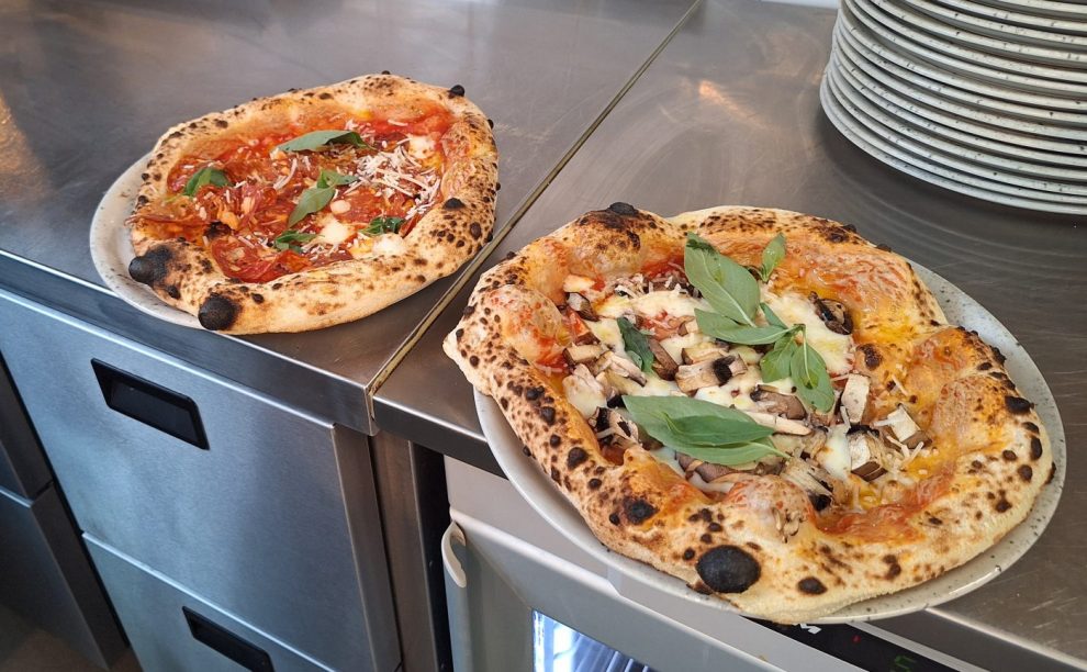 Två pizzor ligger på tallrikar på en rostfri bänk.