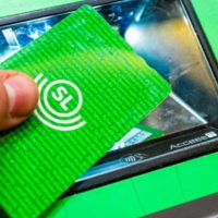 Ett grönt foto där det står SL på som hålls av en hand som lägger kortet på en kortavläsare i genomskinlig plats och grön ram