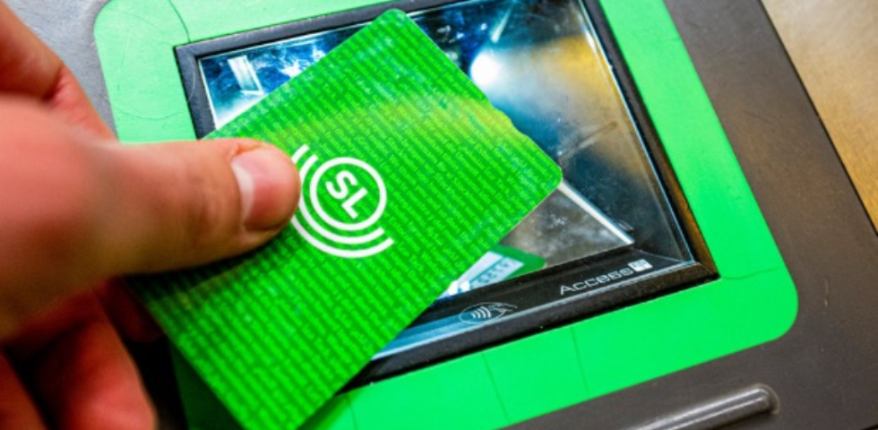 Ett grönt foto där det står SL på som hålls av en hand som lägger kortet på en kortavläsare i genomskinlig plats och grön ram