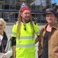 En vit kvinna i blonderat kort hår, i mitten en vit man med långa rastafariflätor och till höger en vit man med hatt.
