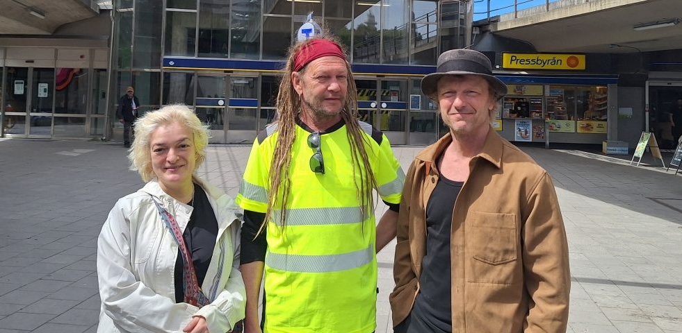 En vit kvinna i blonderat kort hår, i mitten en vit man med långa rastafariflätor och till höger en vit man med hatt.