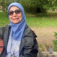 Kvinna som sitter på en parkbänk. Grönska i bakgrunden.