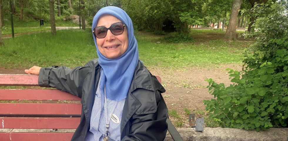 Kvinna som sitter på en parkbänk. Grönska i bakgrunden.