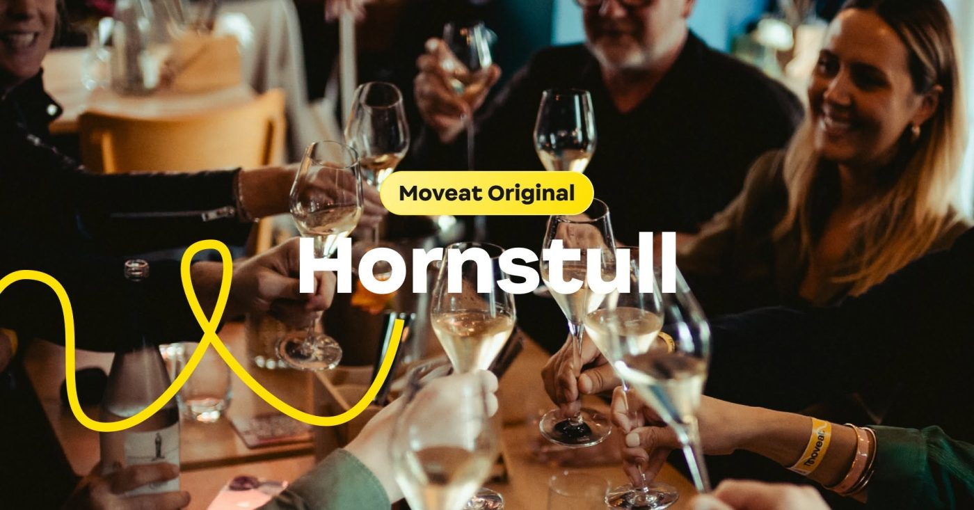 Group of people toasting with wine glasses around a table at a social event, Moveat Original branding visible