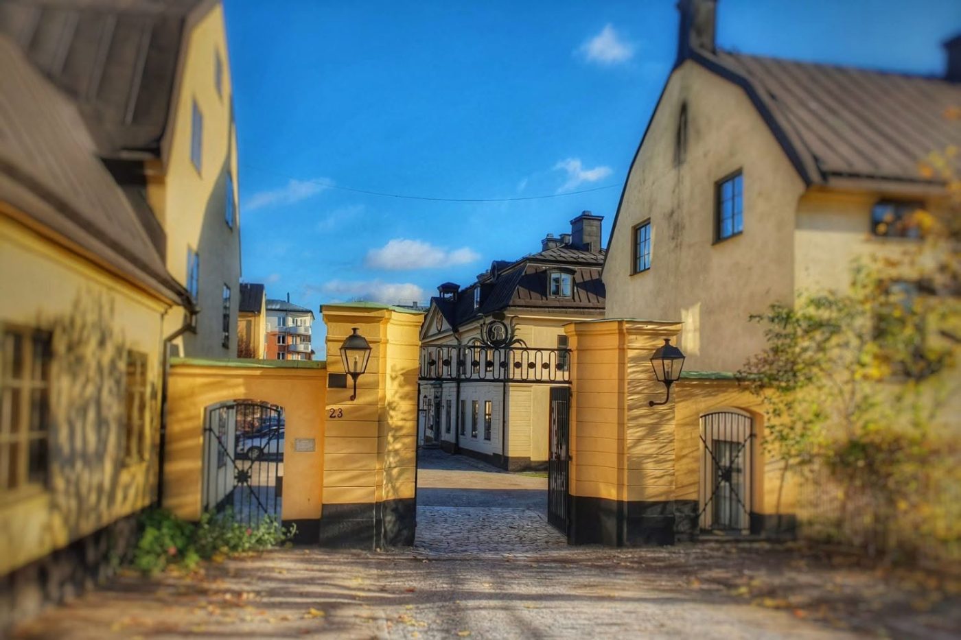 Yellow gate pillars frame a cobblestone courtyard between cream buildings under a bright blue sky.