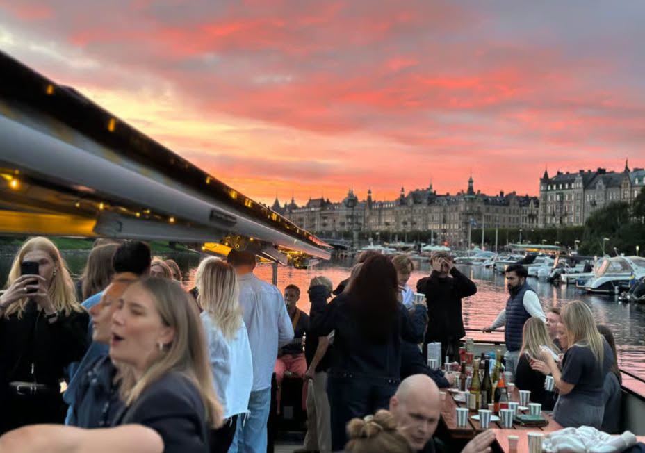 Group of people partying on a boat at sunset with a harbor and historic buildings in the background