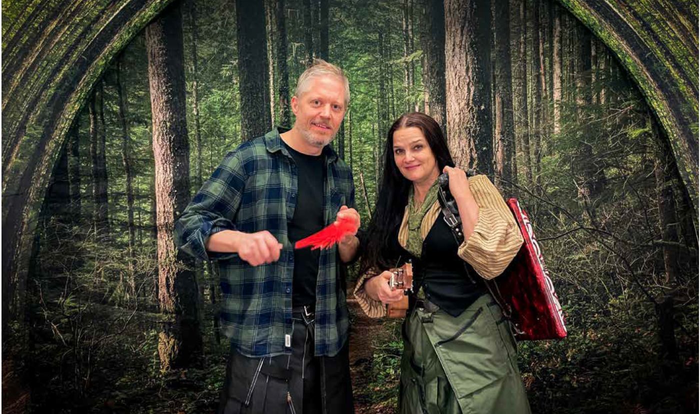 Man and woman pose in front of a forest backdrop; the man holds a bright red parrot toward the camera.